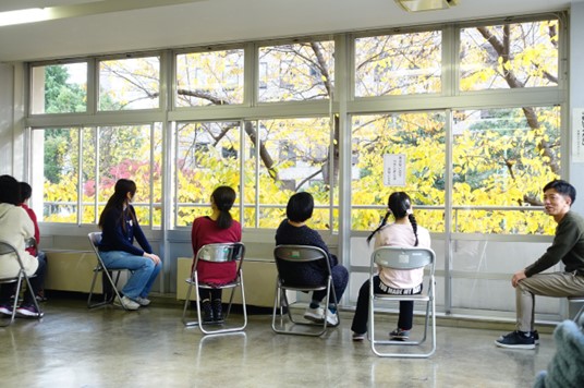 参加者5人が窓際に椅子を置いて座り、窓の外のイチョウを見ている