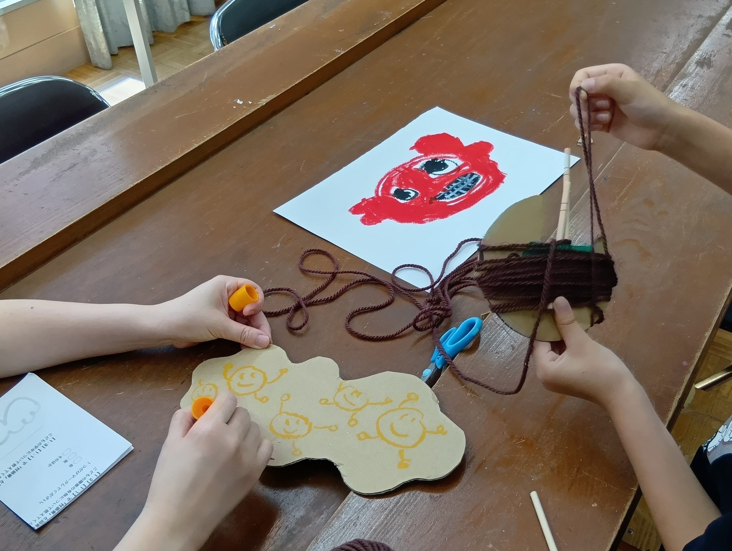赤いキャラクターの絵と、丸いダンボールに茶色い毛糸を巻き付けている様子