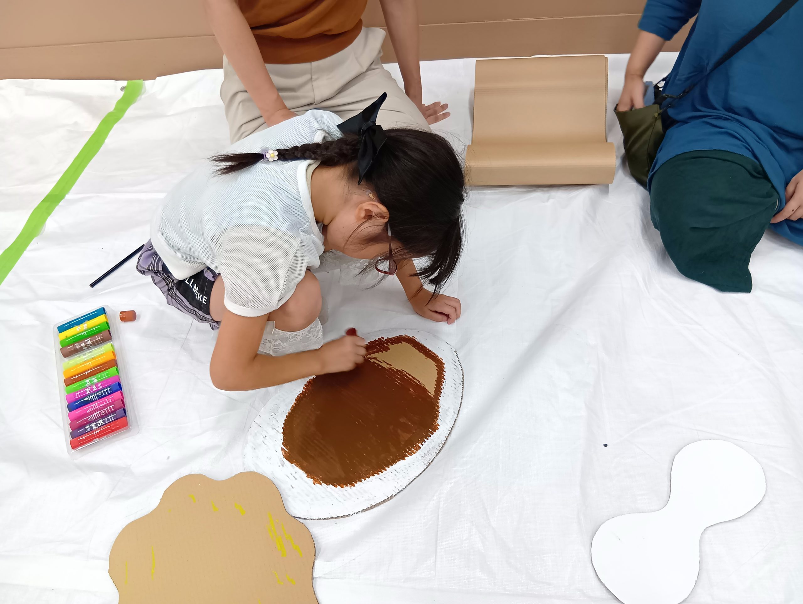茶色いテンペラクレヨンで、楕円の形を描く子ども