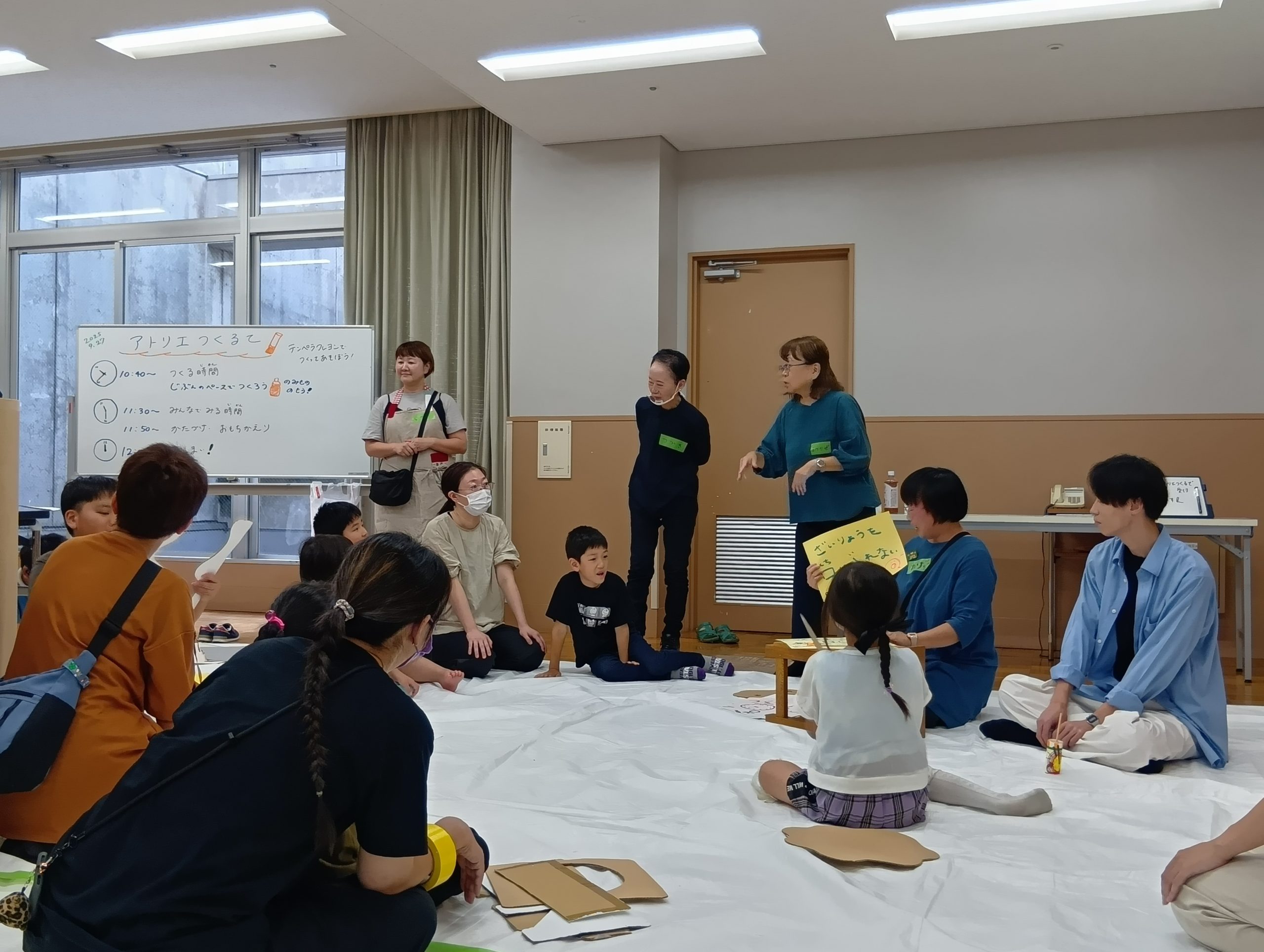 ビニールシートをひいた会場に子どもが座っている。真ん中でファシリテーターが手書きのフリップを使って説明している
