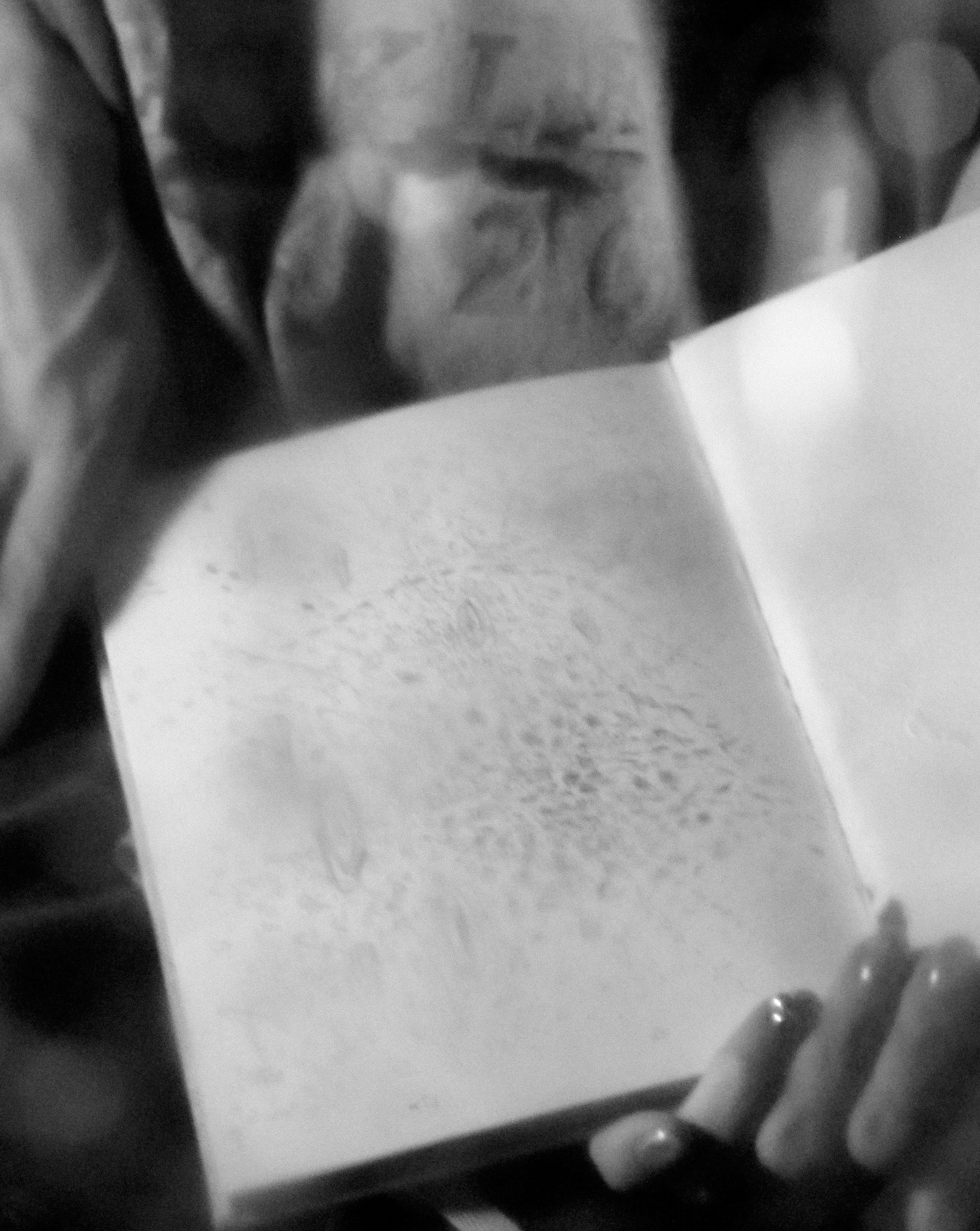 ひらかれた白いノートを手に持つ人影のようなモノクロ写真。ノートには鉛筆で描かれたような絵。