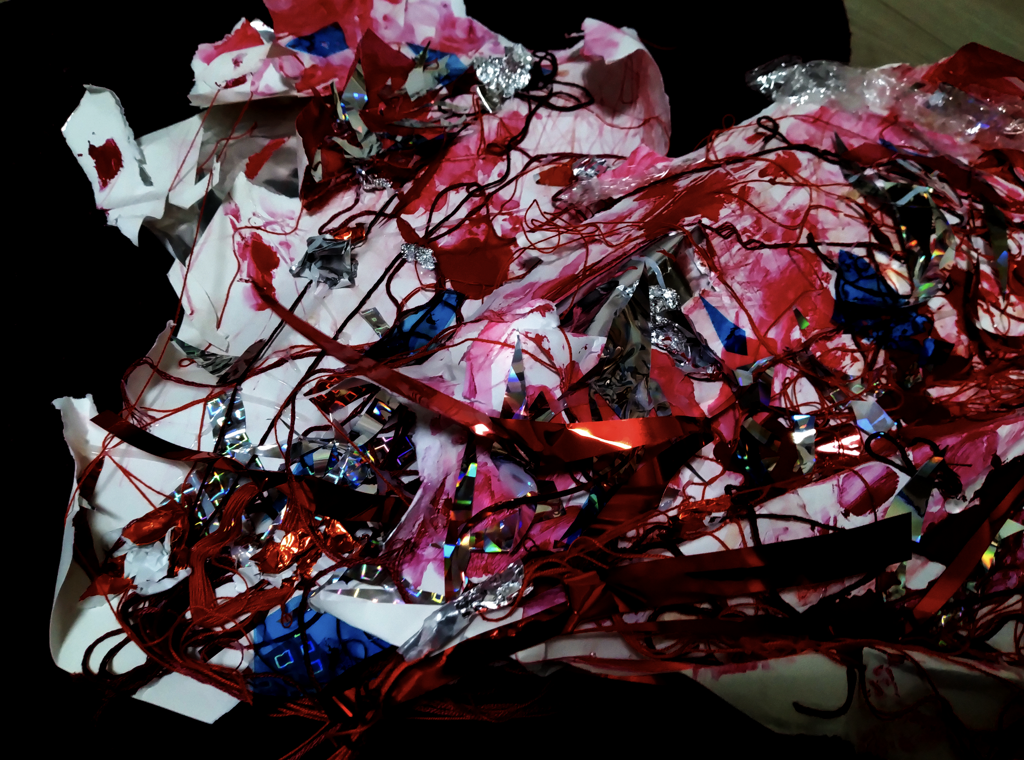 作品画像。白い紙をぐちゃぐちゃにしたりやぶいたりして、その上を赤や青の銀テープや、赤い絵の具がからみあっている。