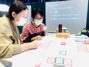 机の上に広げたカードを使って会話する2人の様子。